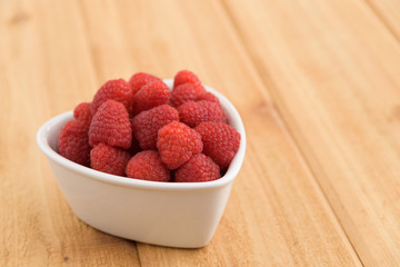 Close-up of fresh red raspberries in a white heart shaped bowl
