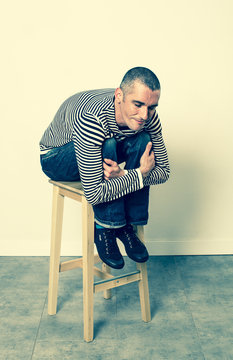 reflection concept - smiling 30s man sitting and leaning forward on a stool relaxing for satisfaction, green effects in studio.