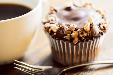 Closeup of a chocolate toffee cupcake and a cup of coffee