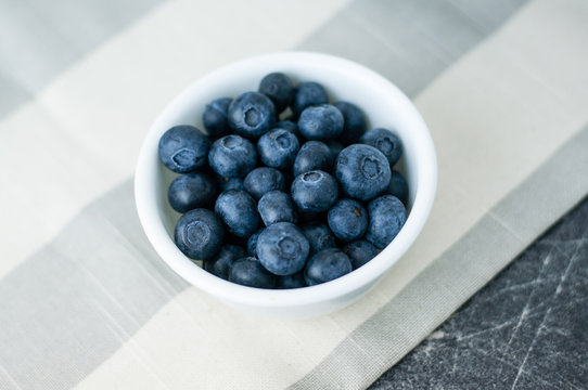 Small white bowl of blueberries linen tablecloth close up top view