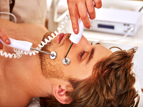 Portrait of handsome man receiving electric facial  therapy hydradermie at beauty salon. 