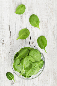 Baby spinach leaves in bowl on white rustic table, organic and healthy food, top view