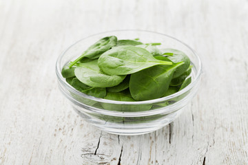 Baby spinach leaves in bowl on white rustic table, organic and healthy food