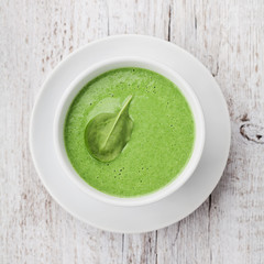 Spinach cream soup in bowl on white rustic table, top view