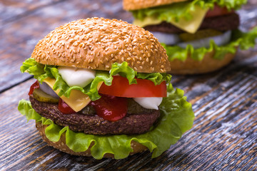Hamburger with beef cutlet, fresh vegetables: tomatoes, onions, lettuce, sauce and bun with sesame seeds on a wooden background