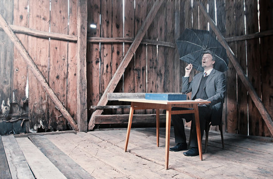 Businessman with Feet on Table Holding Umbrella is Waiting for Better Business