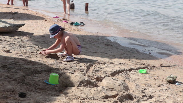 Caucasian small girl builds sandcastle at the sandy beach near a water. The Red Sea, Egypt
