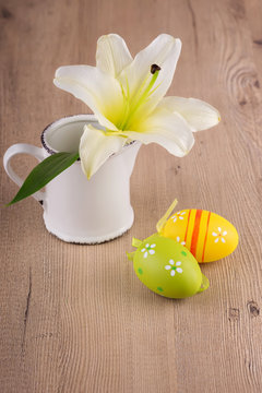 Easter background. Lily flower in a vase with easter eggs on a wooden background.