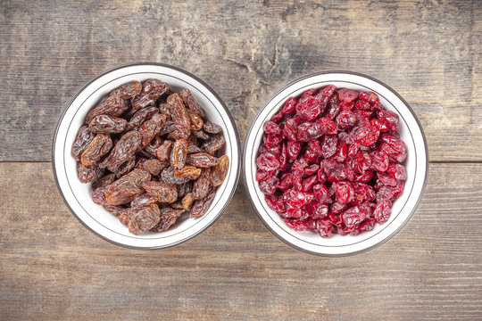 Dried cranberries and raisins in bowls on wooden background