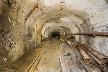 Old abandoned iron mine tunnel passage with rails, wood boards, pipes