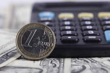 coin euro closeup, calculator on the background of banknotes dollars