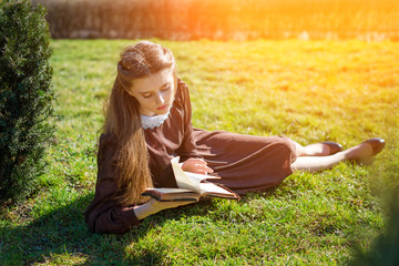 Romantic young woman reading a book in the garden sitting on the grass. Relax outdoor time concept.