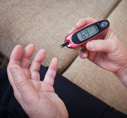 Medicine, diabetes, glycemia, health care and people concept - close up of woman checking blood sugar level by glucometer and test stripe at home