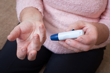 Medicine, diabetes, glycemia, health care and people concept - close up of woman checking blood sugar level by glucometer and test stripe at home