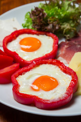 Two fried eggs with ham, vegetables and cheese served on a white plate, ready for consumption
