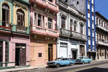 Fototapeta na wymiar Kuba, Havanna, nahe Malecon: Zwei parkende Oldtimer in typische Strassenszene mit verfallenen Häusern Fassaden im Zentrum der kubanischen Hauptstadt der karibischen Insel