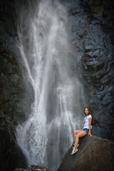Fototapeta na wymiar girl on rock with waterfall background