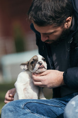 Handsome, bearded, middle age man enjoying outdoors with his adorable French bulldog puppy. City park in background.