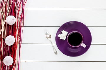 cup of tea or coffee on violet plate, silver spoon,  lump sugar, marshmallow on violet purple dry decor straw on white colored wooden table,  top view