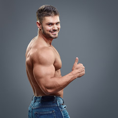 Muscular man shows thumbs up on grey background