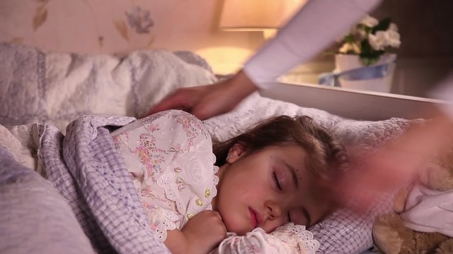 Mother puts her little daughter to bed and turns off the light in the bedroom
