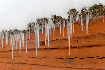 Icicles hanging from a snowy roof on a red barn