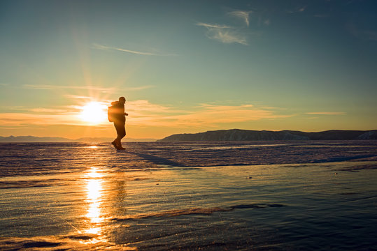 Silhouette of young traveller photographer going on the Baikal lake ice in winter on a sunset