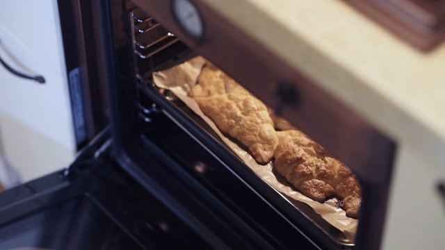 Women's hands removing hot pastry from an oven