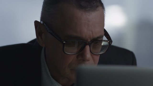 elderly businessman working with computer in modern office.  he takes off his glasses and peers at the screen