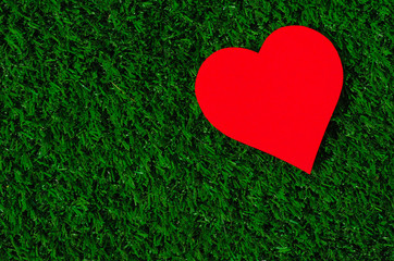 Holiday card: red paper heart lies on a green grass