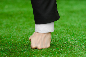 Nature and business topic: the hand of man in a black suit presses his fist green grass