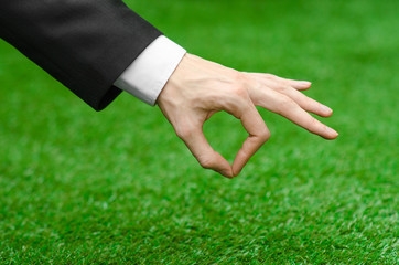 Nature and business topic: the hand of man in a black suit showing gesture ok on a background of green grass