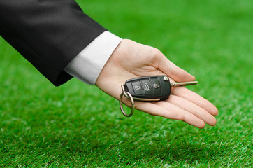 The new machine and a business topic: hand in a black suit holds the keys to the new car on a background of green grass