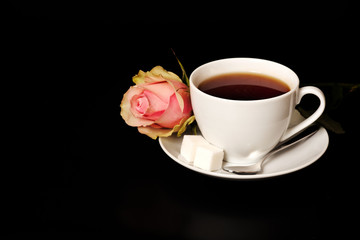 White cup of tea on the black background table with red rose