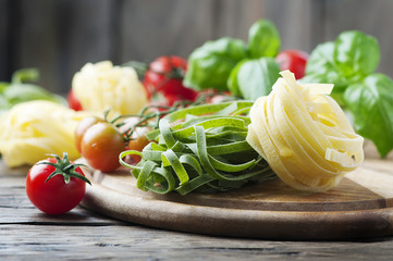 Raw pasta, tomato and basil on the wooden table