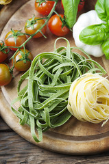 Raw pasta, tomato and basil on the wooden table