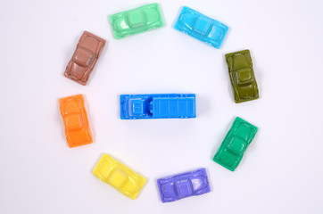 Colorful plastic toy cars on a white background. Many cars surrounded one car. Dense urban city traffic. Concept. Close up view, flat lay. 