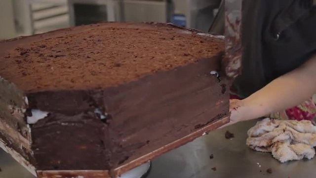 Close up of chocolate frosting being smoothed on a triple layer wedding cake