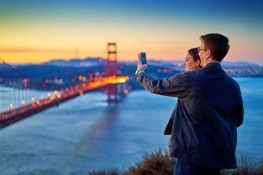 couple taking photo in front of golden gate bridge at sunrise
