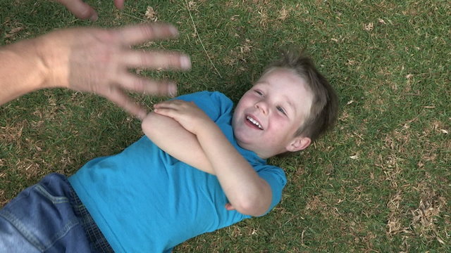 Four year old child lying on grass laughing and being tickled by mother