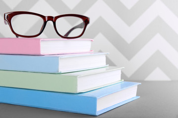 Books and eyeglasses on grey table against ornament wall, close up