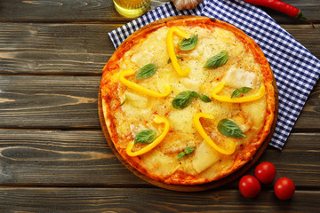 Tasty pizza decorated with basil and pepper on wooden background
