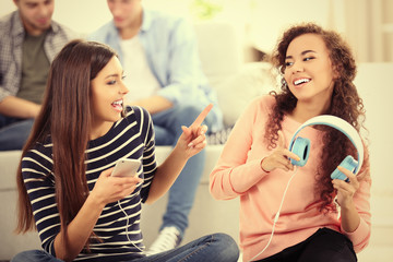 Two teenager girls listening to music with headphones in living room