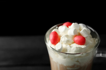 Cup of coffee with whipped cream and candies on black background