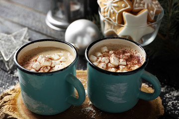 Two mugs of hot cacao with marshmallow and cookies on black table