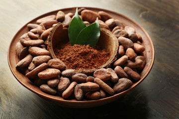 Bowl with aromatic cocoa harvest on wooden background, close up