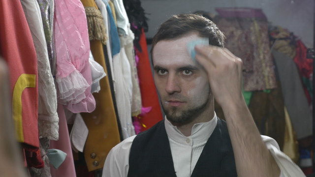 Handsome young male actor applying white face cream for mime make-up