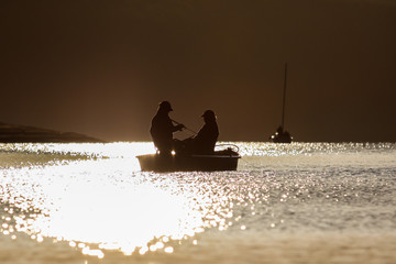 Boot auf dem Wasser mit zwei Anglern bei Sonnenuntergang im Gegenlicht