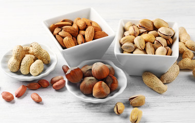 Naklejka na ściany i meble Pistachios, almonds, hazelnuts, peanuts and walnut kernels in the ceramic bowls, on white wooden backgrounds