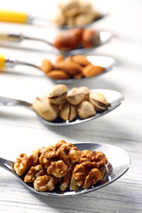 Pistachios, almonds, hazelnuts, peanuts and walnut kernels in the metal spoons, on white wooden background